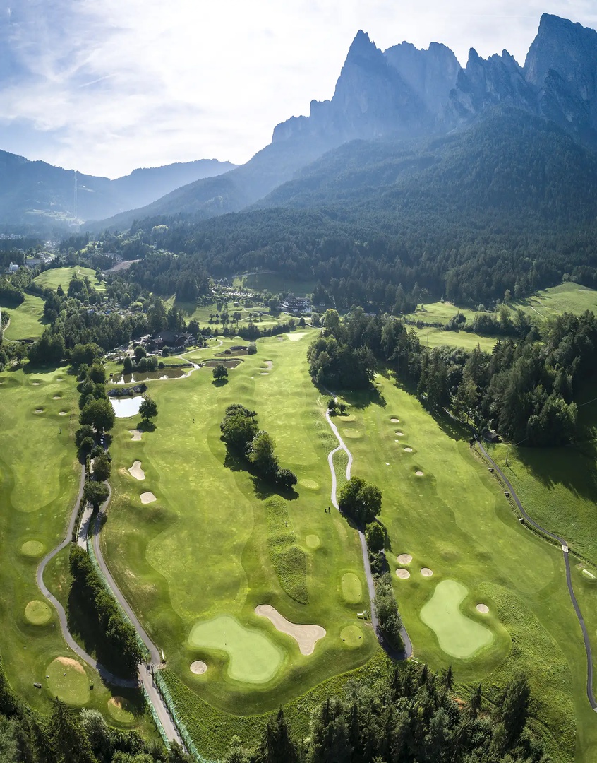 18-Loch-Golfplatz St. Vigil Seis Panorama Blick von oben auf den Golfclub St. Vigil Seis, im Hintergrund die Dolomiten
