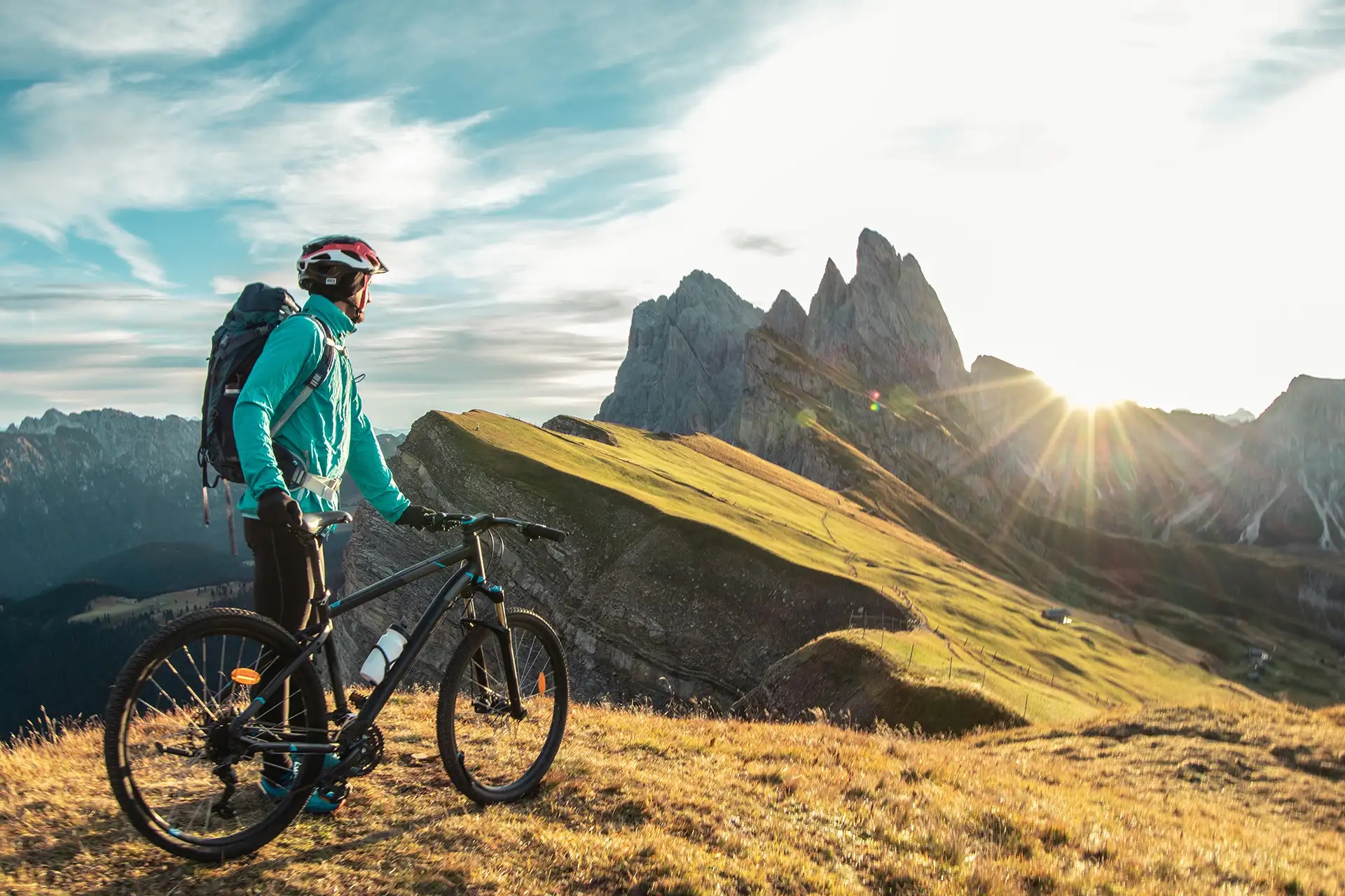 Junger Mann mit Mountainbike auf dem Gipfel des Seceda bei Sonnenaufgang. Puez Odle, Trentino, Dolomiten, Italien.