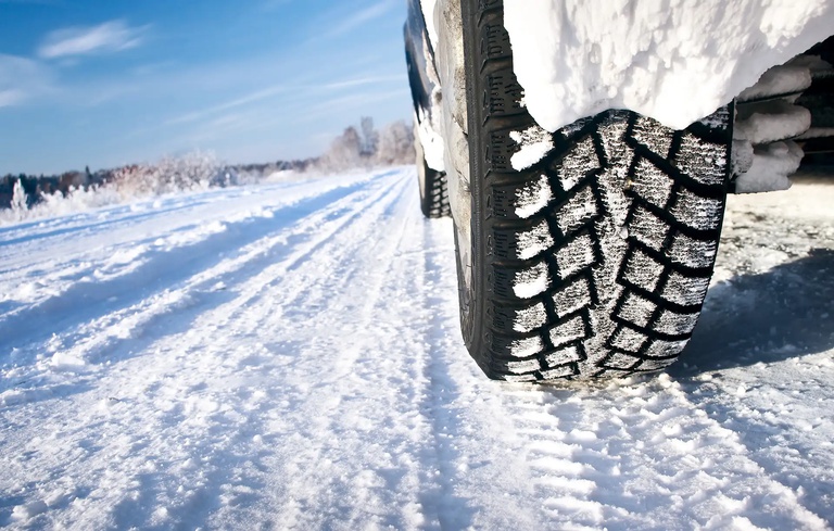 Winterreifenpflicht in Italien Nahaufnahme eines Autoreifens mit Winterprofil auf verschneiter Straße bei klarem Himmel – ideal zur Veranschaulichung von Winterreifen im Einsatz bei winterlichen Straßenverhältnissen.